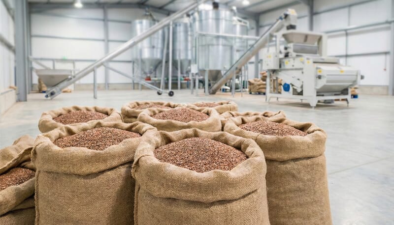 Large jute sacks filled with raw brown flaxseeds in a clean industrial factory warehouse, illustrating bulk oil production capacity.