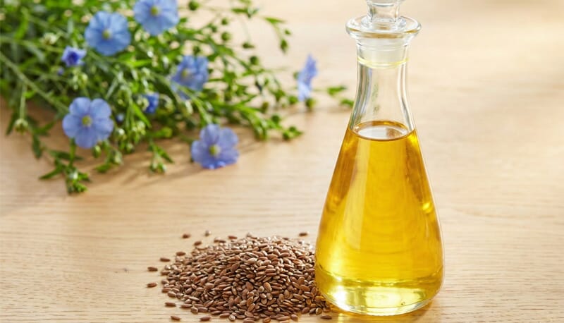 Translucent, grade-A refined flaxseed oil in a glass carafe displayed next to raw seeds, showing high clarity and Omega-3 quality.