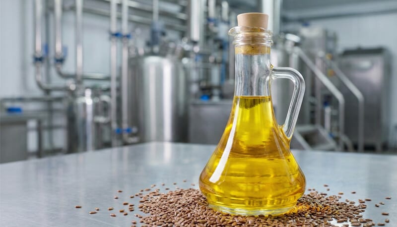 Bottle of freshly extracted cold-pressed flaxseed oil sitting on a stainless steel work surface inside a modern Guance Machinery oil processing plant.