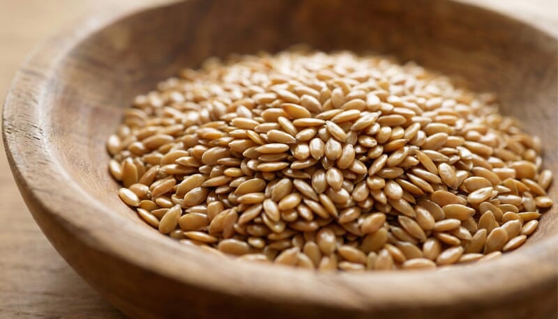Macro close-up detail of high-quality golden flaxseeds texture, ready for cold press oil extraction.